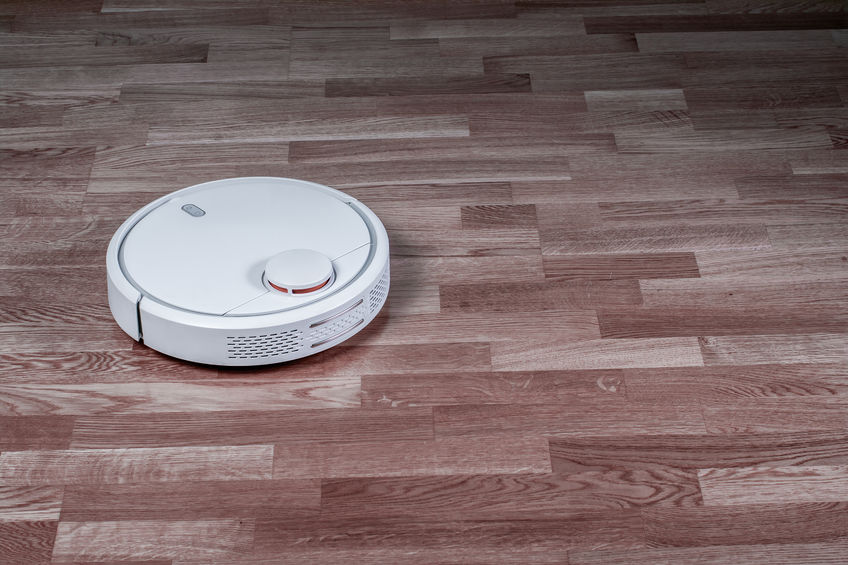 White robotic vacuum cleaner runs on laminate floor. Robot controlled by voice commands for direct cleaning. Modern smart appliance for cleaning house