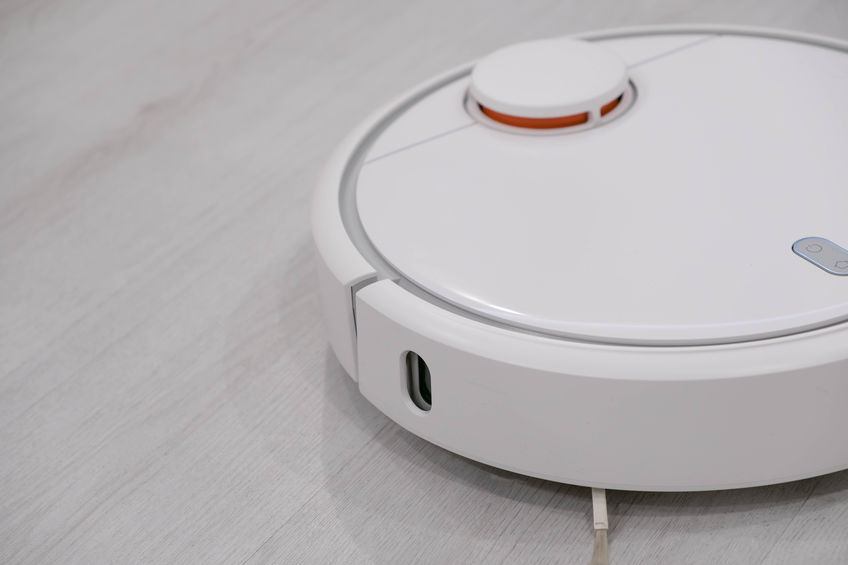 White robotic vacuum cleaner on laminate floor cleaning dust in living room interior. Smart electronic housekeeping technology.